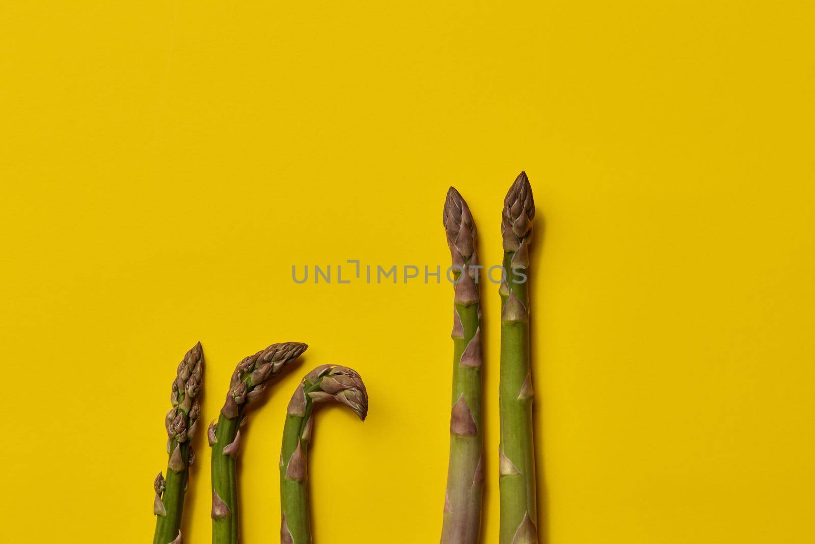 Raw uncooked green asparagus spears on yellow background. Concept of healthy nutrition, food and seasonal vegetables harvest. Close up, copy space. Flat lay, top view