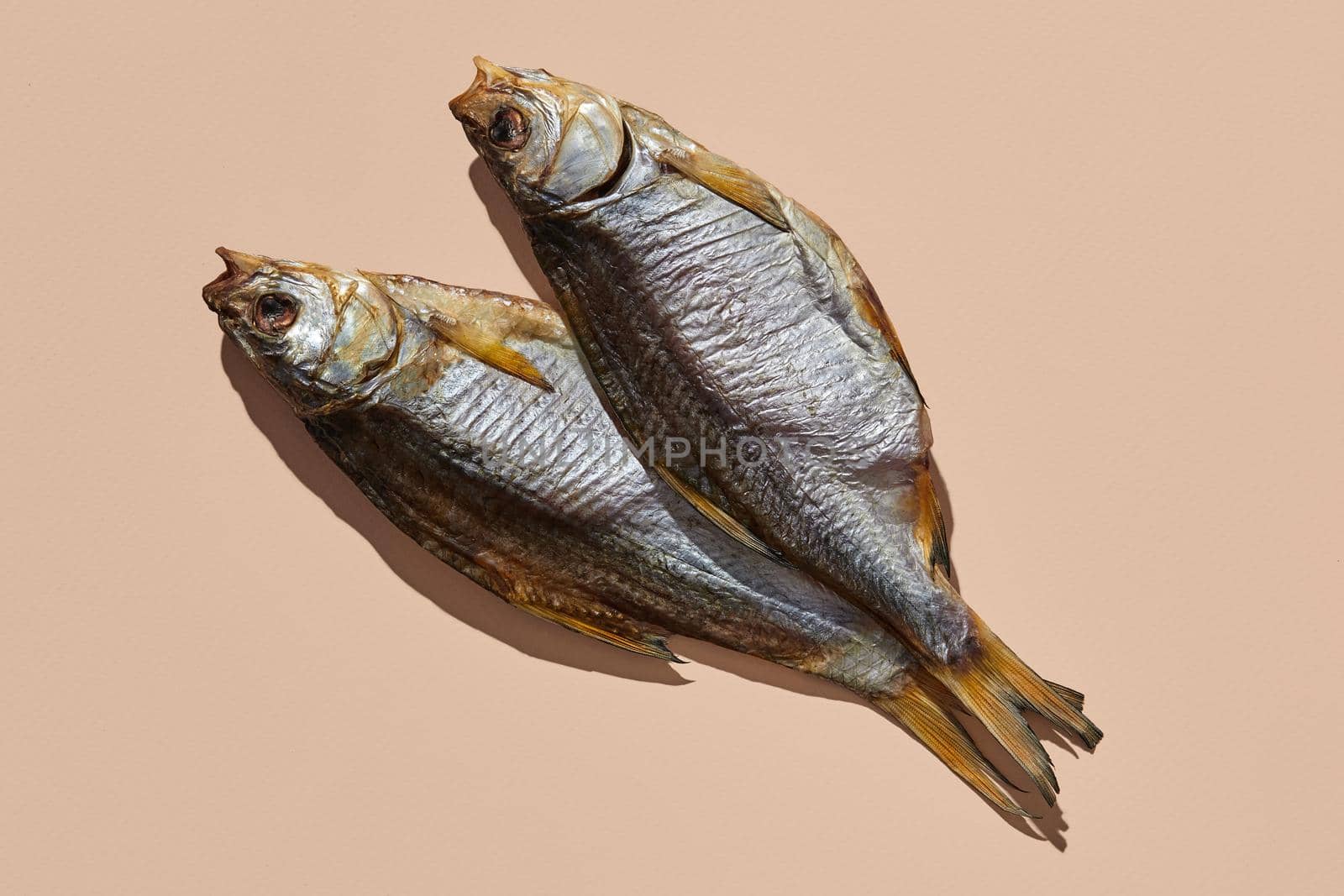 Two dried or jerky salty taranka, yummy clipfish on pink background. Popular beer appetizer. Traditional way of preserving fish. Close up, copy space, top view