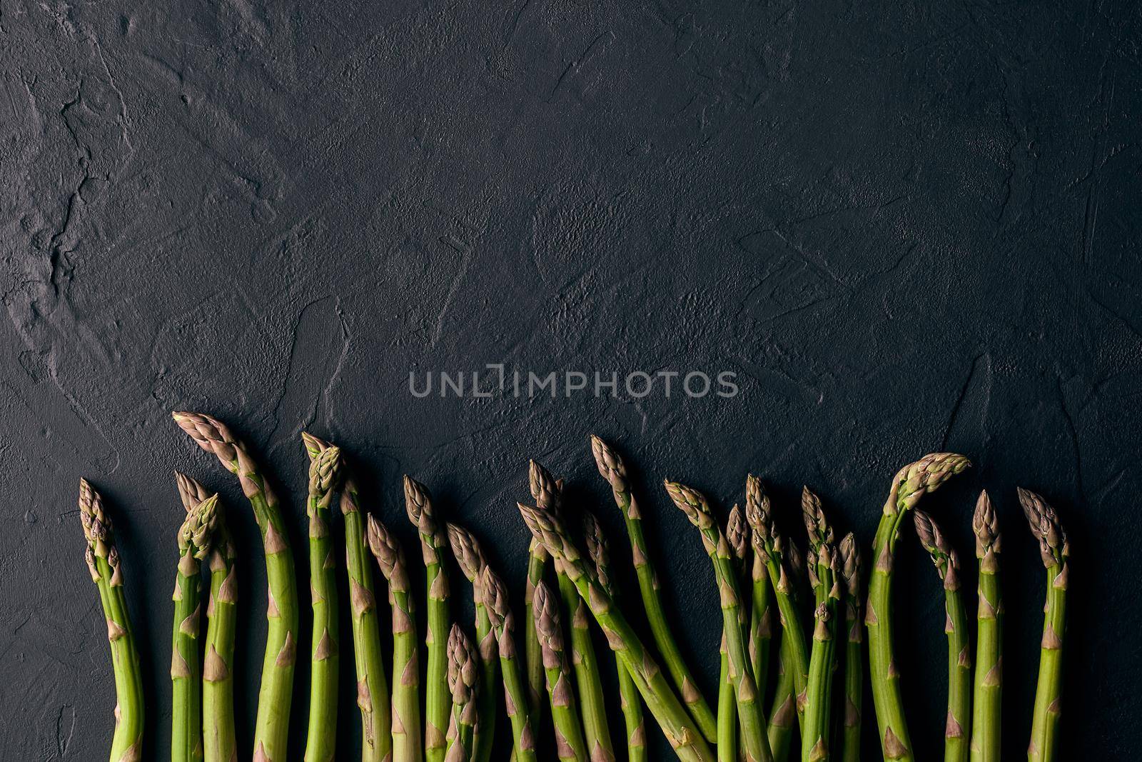 Raw fresh green asparagus stalks over black slate background. Concept of food and seasonal vegetables harvest. Close up, copy space by nazarovsergey