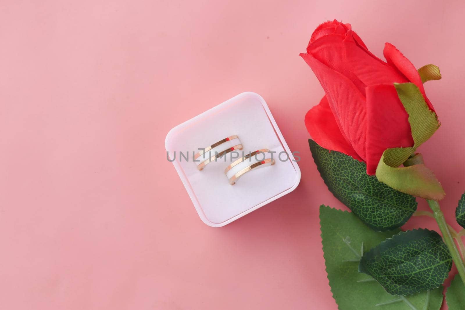 wedding ring and gift box and rose flower on red .