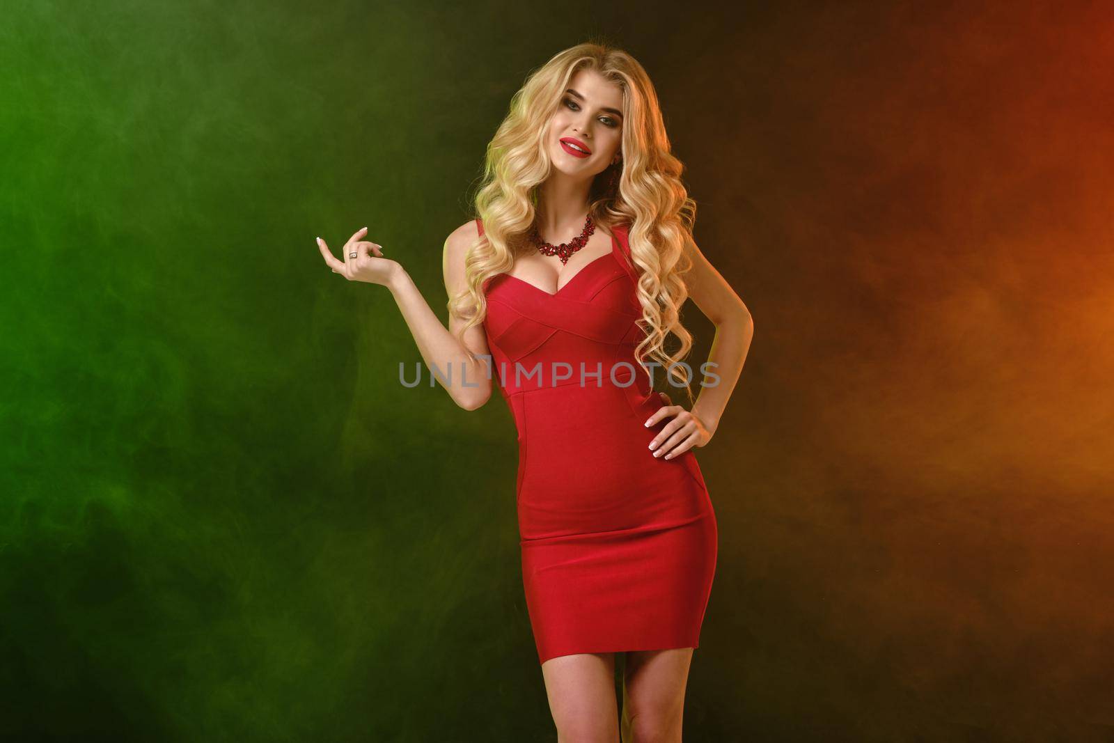 Blonde model in red fitting dress, necklace. Smiling, holding something. Posing on colorful smoky background. Template or mockup. Close up by nazarovsergey