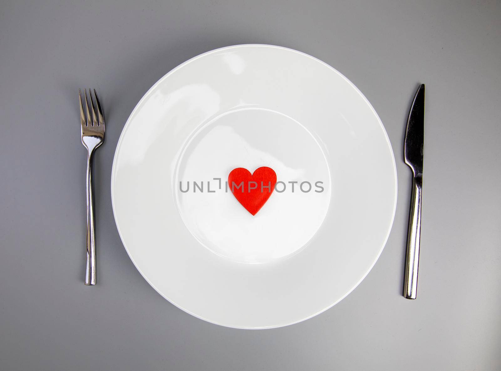 White plate with, fork and knife, red heart on grey background, flat lay. Valentine's day or medical health concept top view by Annebel146