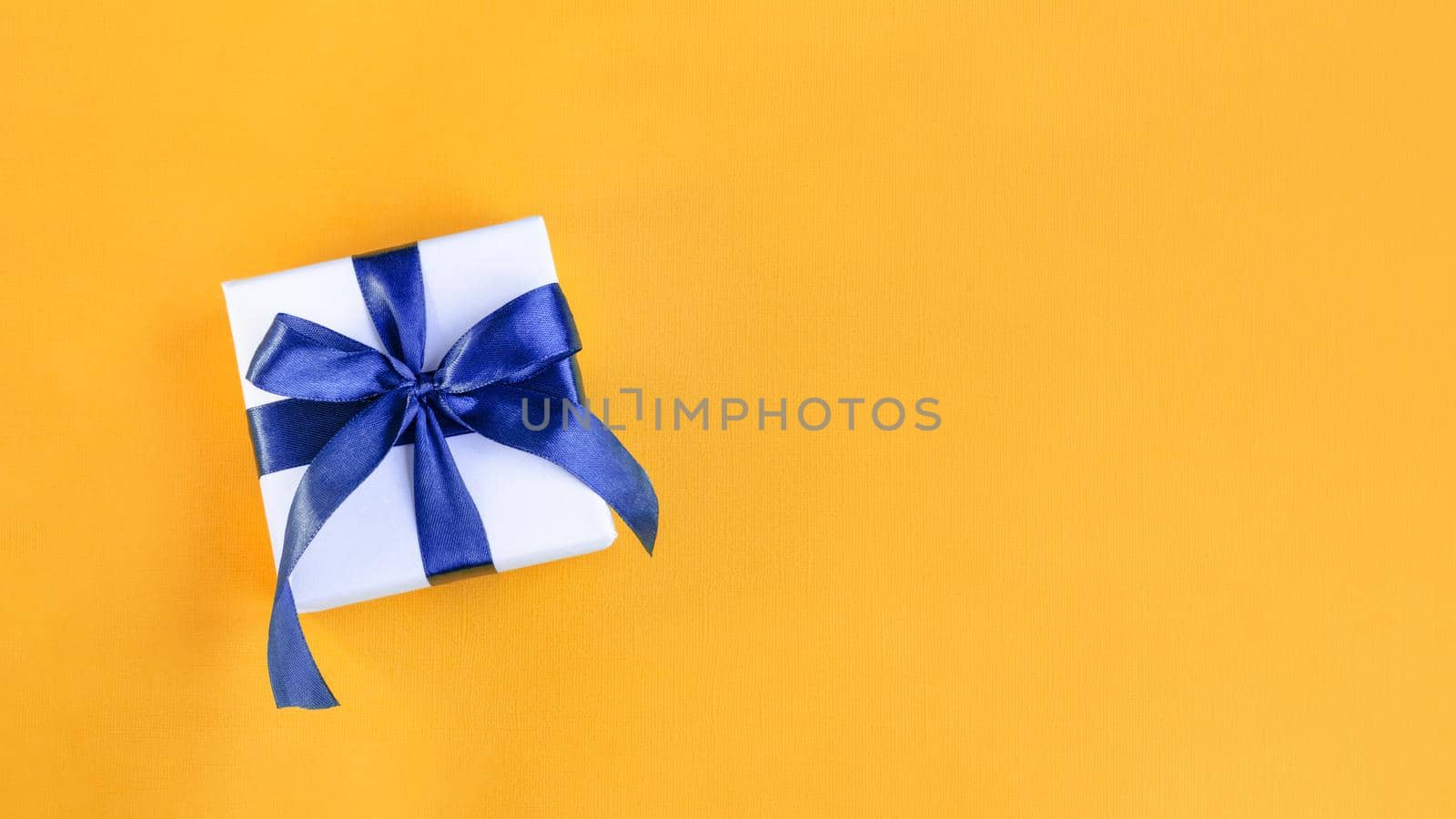 Banner of a Gift wrapped in white paper with a blue bow made of satin on festive yellow orange background by lavsketch