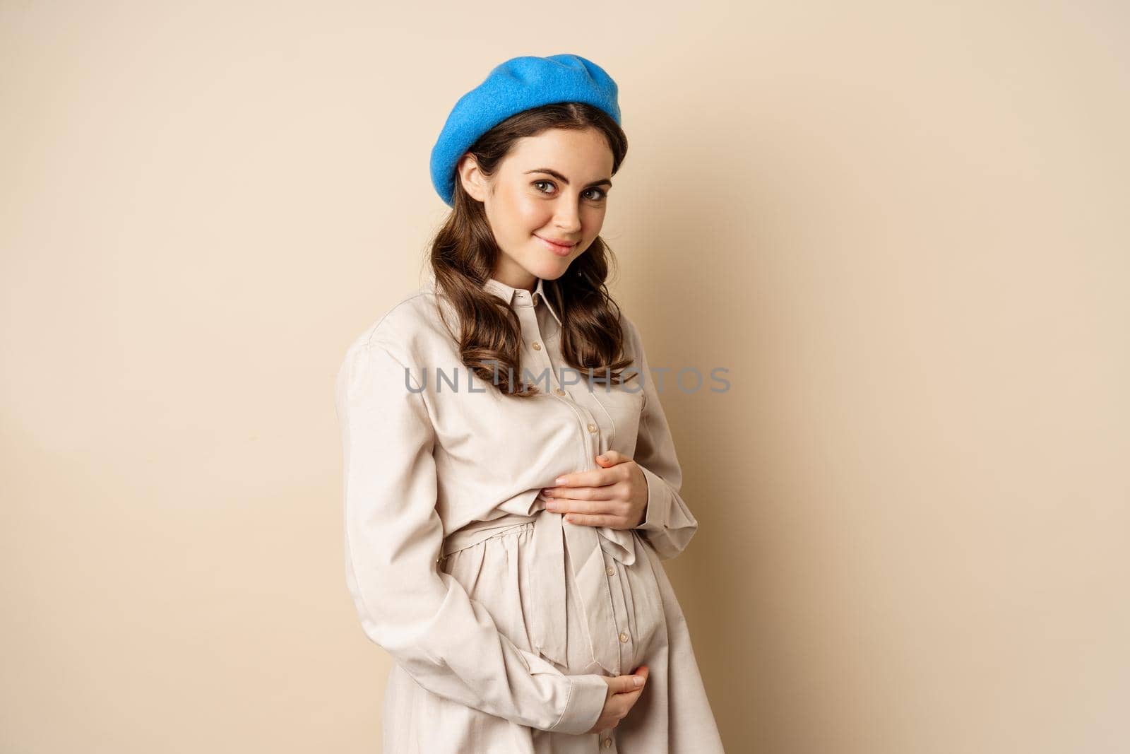 Image of a beautiful young pregnant smiling woman posing isolated over beige background.