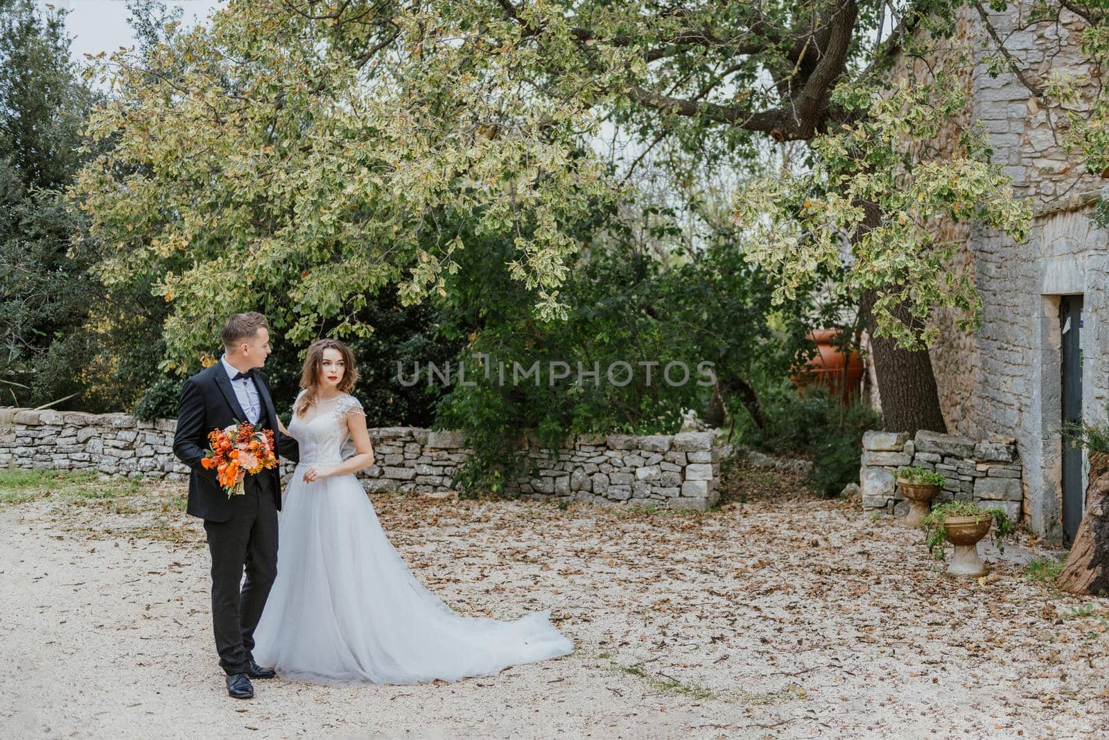 Happy stylish smiling couple walking in Tuscany, Italy on their wedding day. The bride and groom walk down the street by the hands. A stylish young couple walks. Husband and wife communicate nicely. Lovers run through the streets of the city.