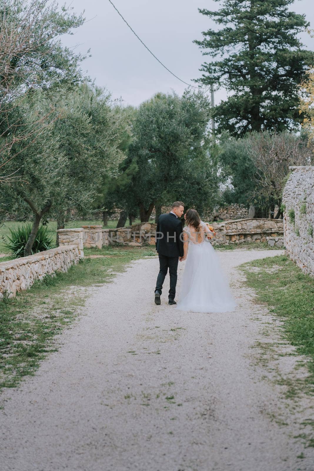 Happy stylish smiling couple walking in Tuscany, Italy on their wedding day. The bride and groom walk down the street by the hands. A stylish young couple walks. Husband and wife communicate nicely. Lovers run through the streets of the city by Andrii_Ko