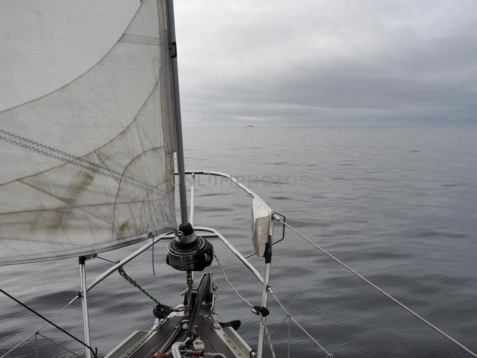 View from bow of yacht sailing in calm water towards small islands under heavy cloudy sky
