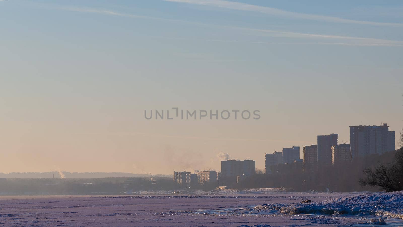 Coast of the winter river in Siberia. Skyline with outlines of houses and steam above the water