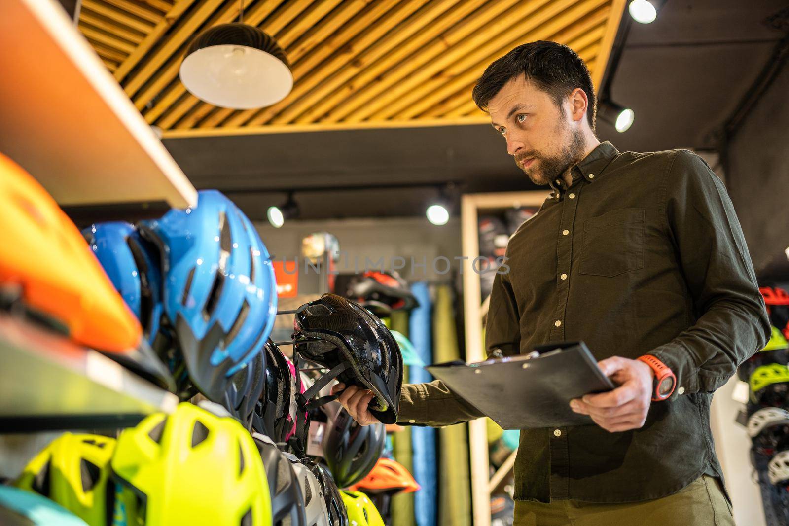 Bike shop manager checks helmet price information on tablet, seller makes an inventory in sports shop. Theme of small business selling bicycles. Seller in hands document checklist in bicycle store.