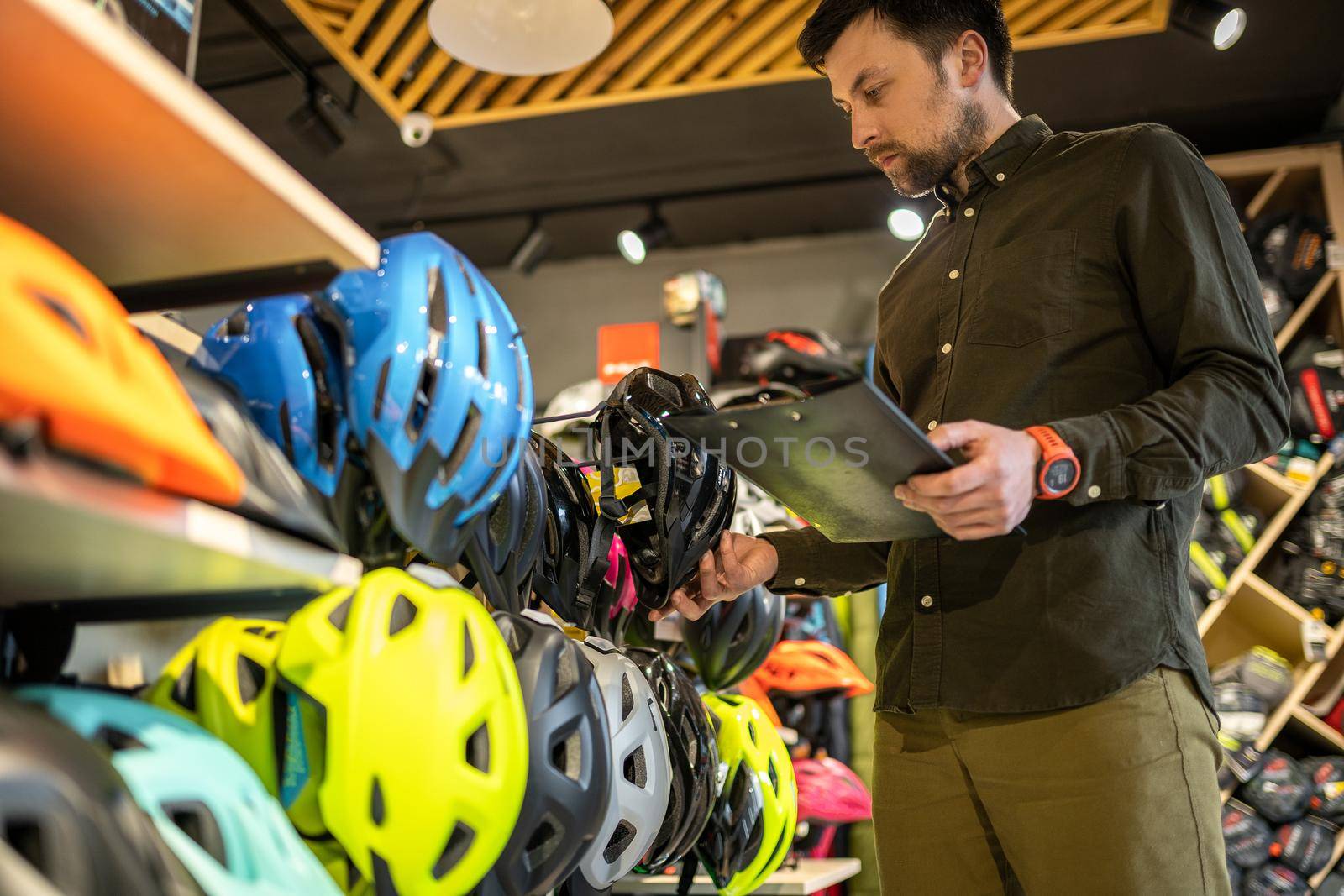 Bike shop manager checks helmet price information on tablet, seller makes an inventory in sports shop. Theme of small business selling bicycles. Seller in hands document checklist in bicycle store.