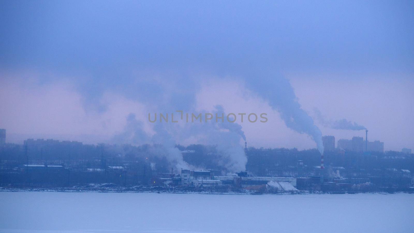 Chimneys smoke in winter against the background of the city and the sky.