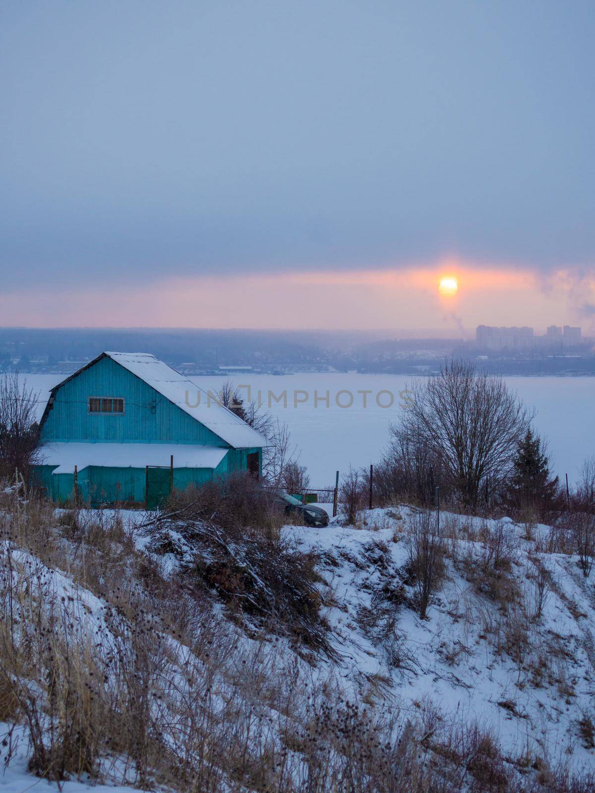 Green wooden house on the background of the river sunset and city in winter