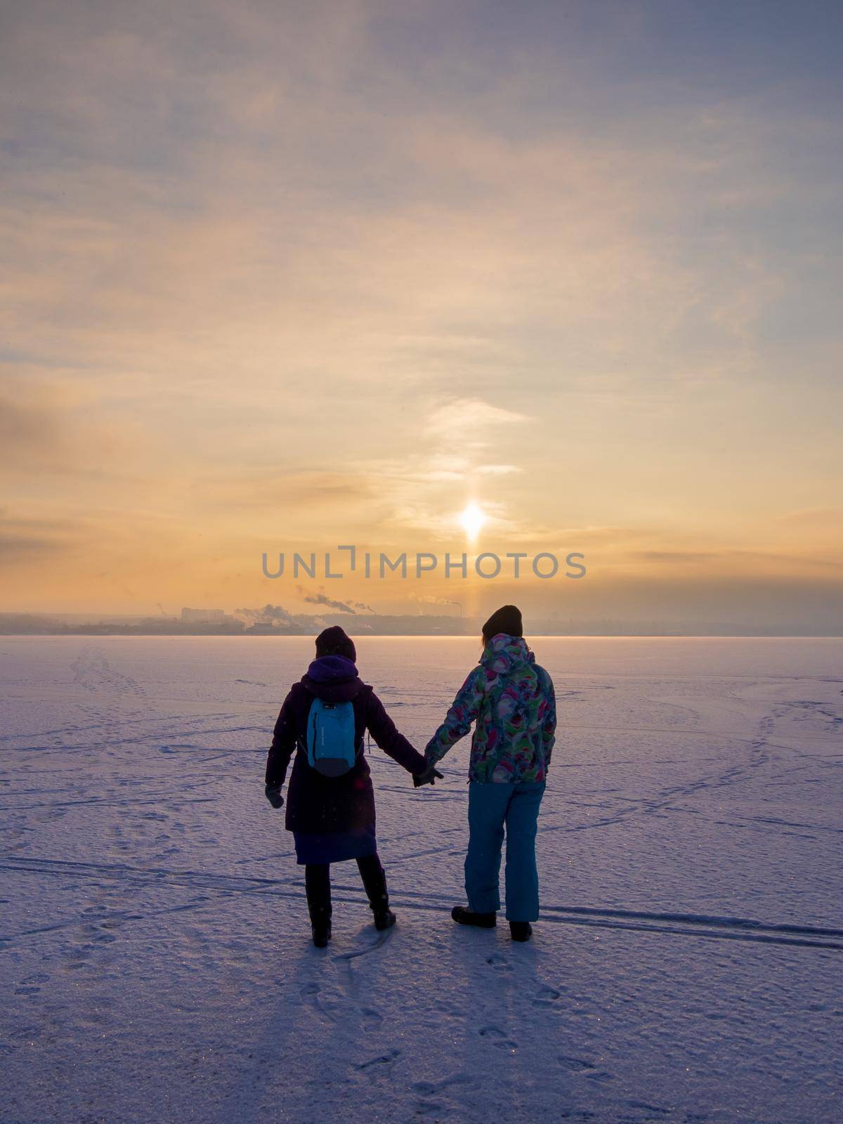 Two girls go into the sunset along the frozen river