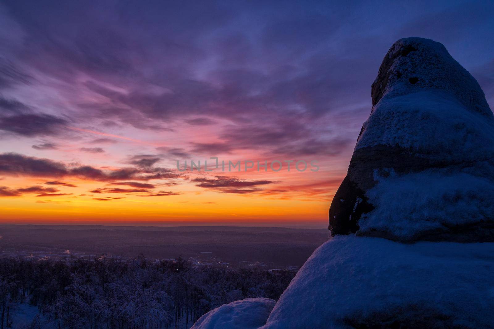 Epic red sunset over the rocks and stones of Ural mountains covered with snowy pines