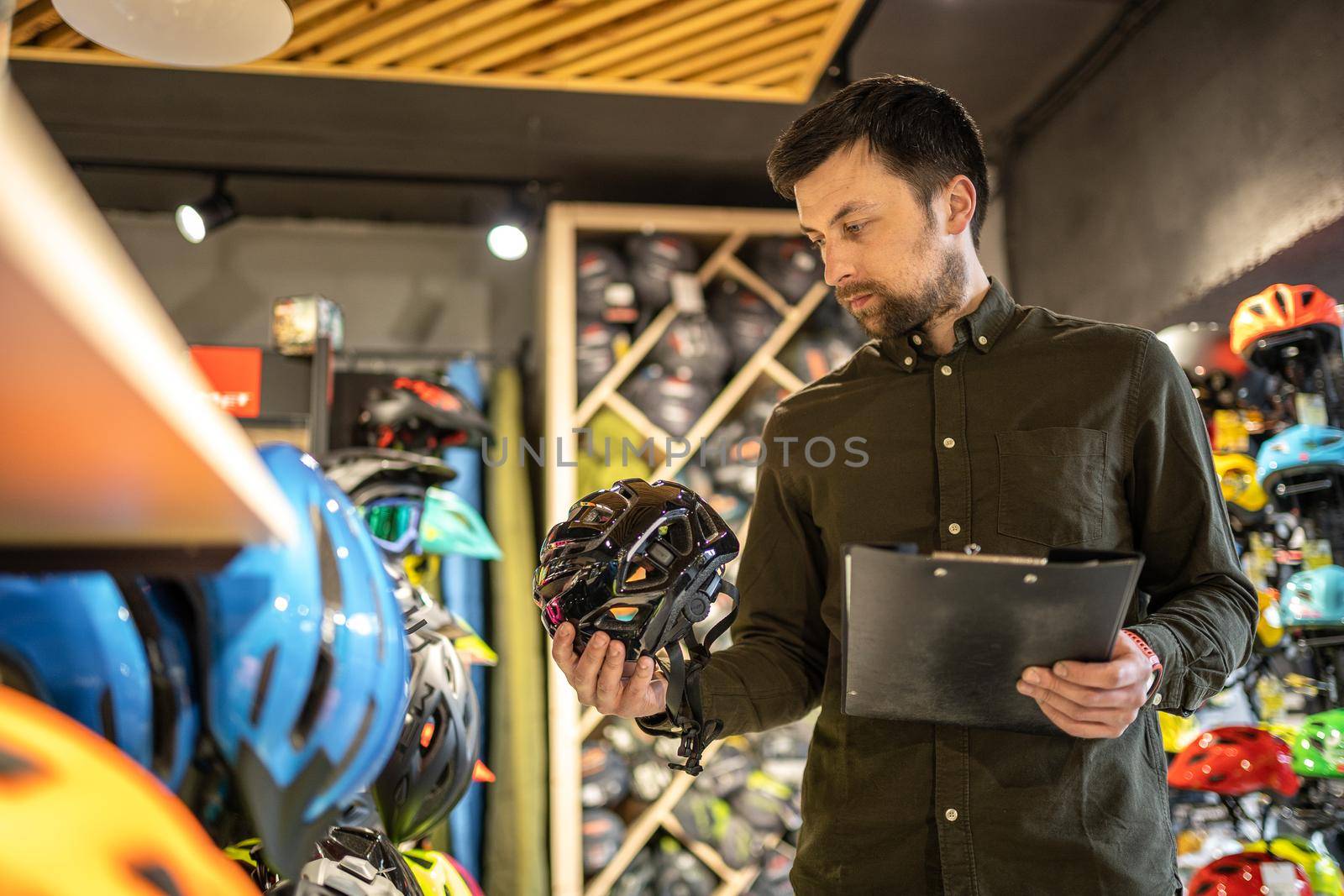 Bike shop manager checks helmet price information on tablet, seller makes an inventory in sports shop. Theme of small business selling bicycles. Seller in hands document checklist in bicycle store by Tomashevska