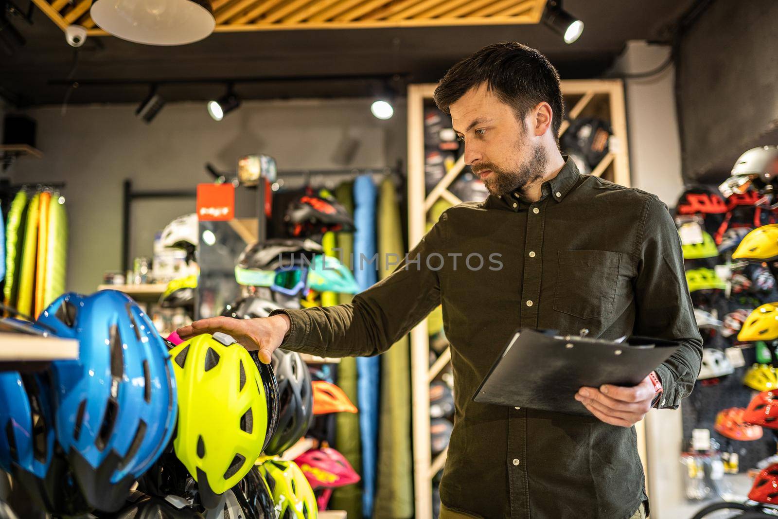 Bike shop manager checks helmet price information on tablet, seller makes an inventory in sports shop. Theme of small business selling bicycles. Seller in hands document checklist in bicycle store.