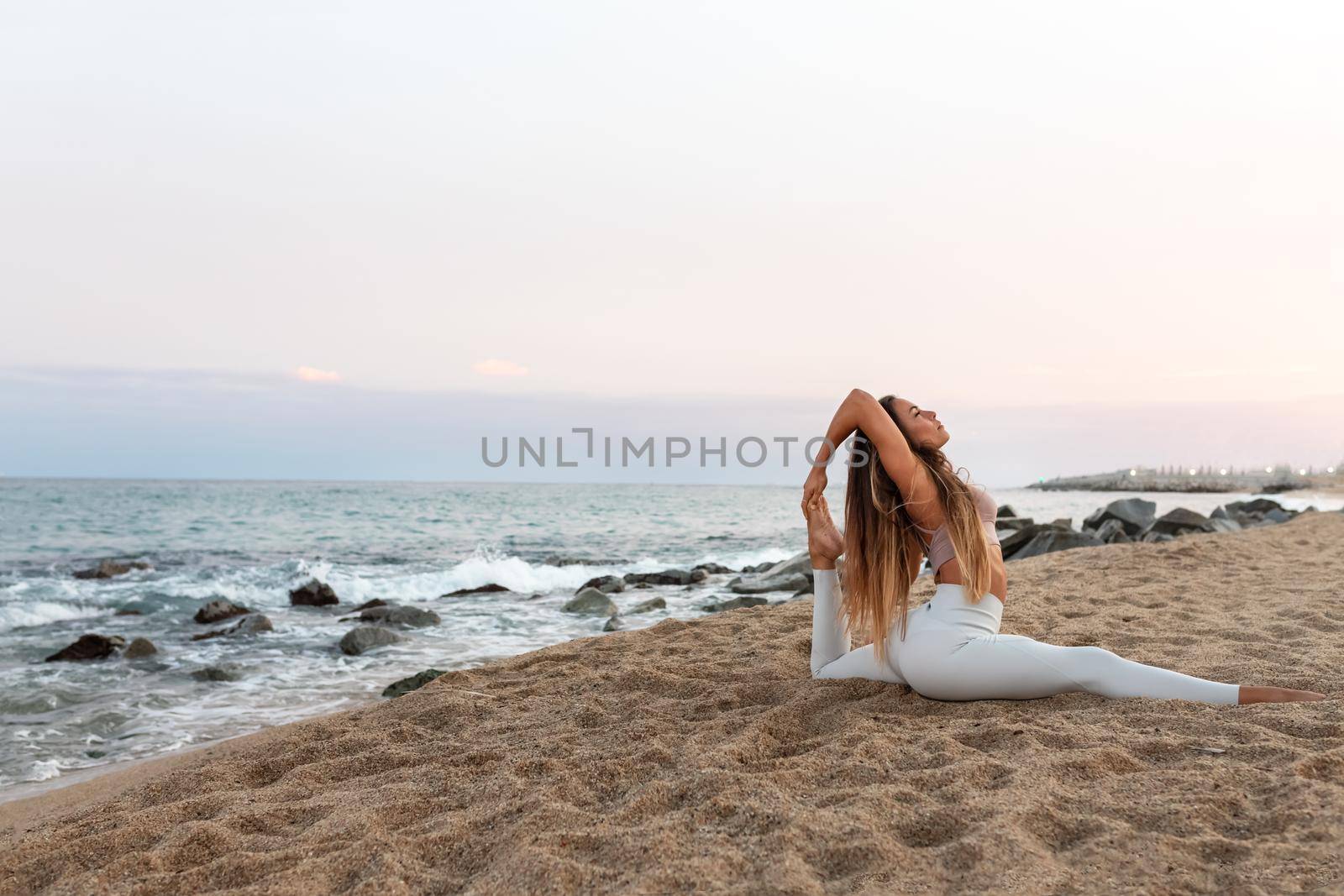 Young flexible caucasian woman practicing yoga on the beach at sunset. Copy space. by Hoverstock
