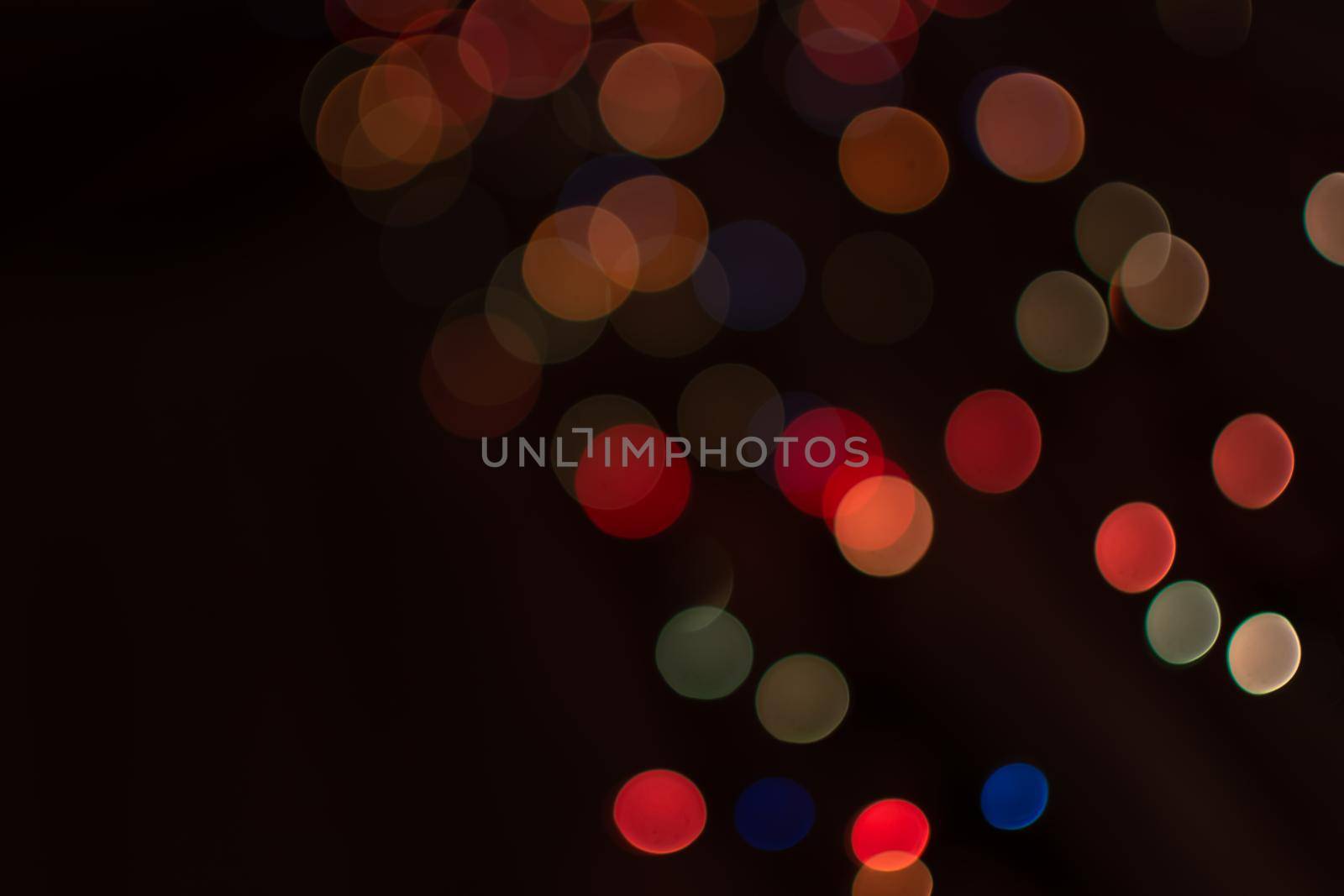 Multicolored bokeh from light garlands on a dark background. Festive background.