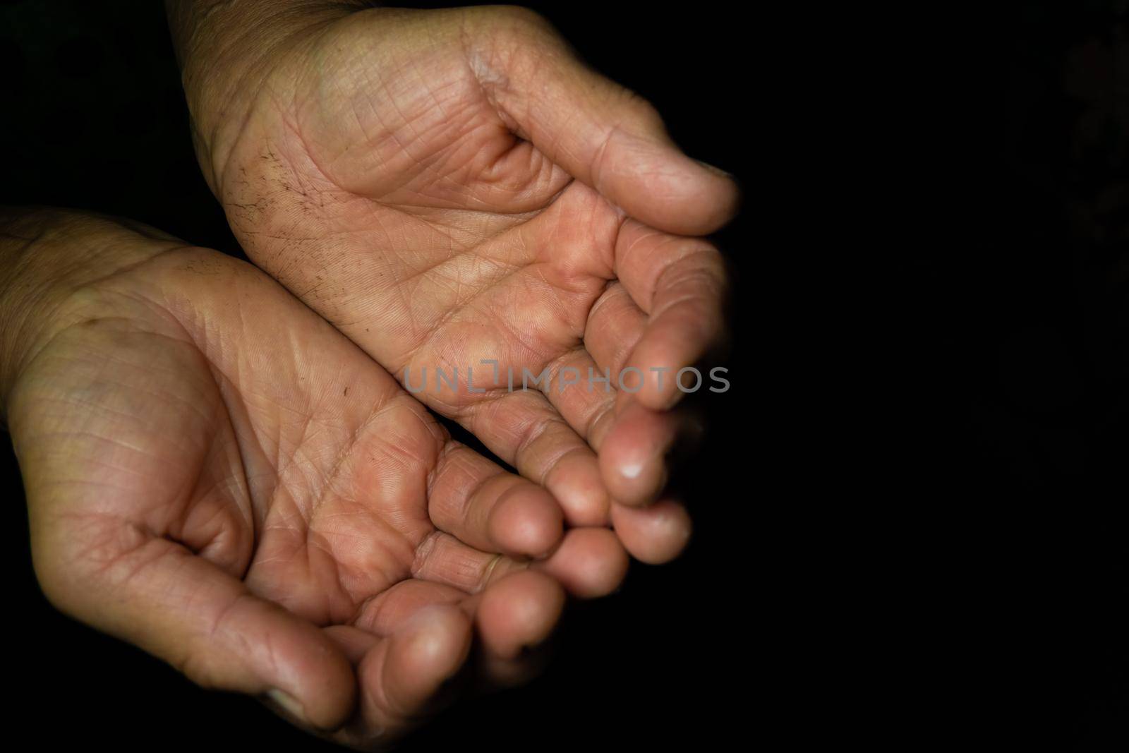Close-up, Two chubby hands with wrinkled palms towards the top of an old woman on a black background with copy space. Grandma begs for help with open palms.