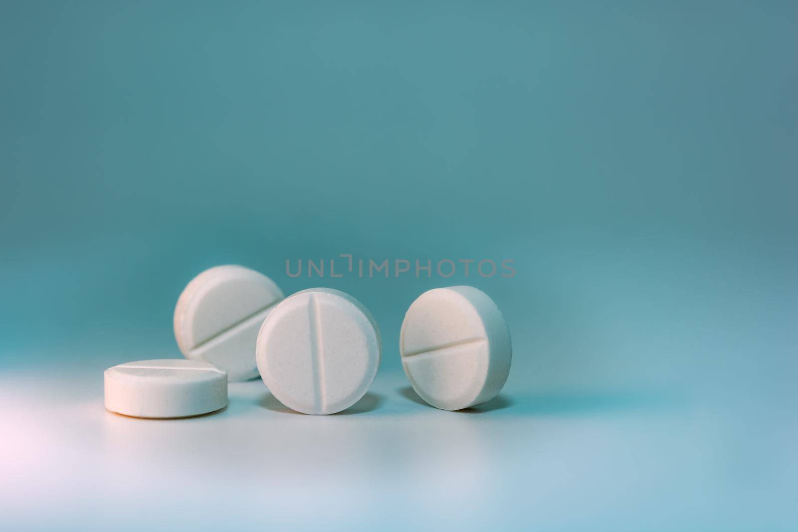 Four white pills on a blue-green background with turquoise. Selective focus. Place for your text.