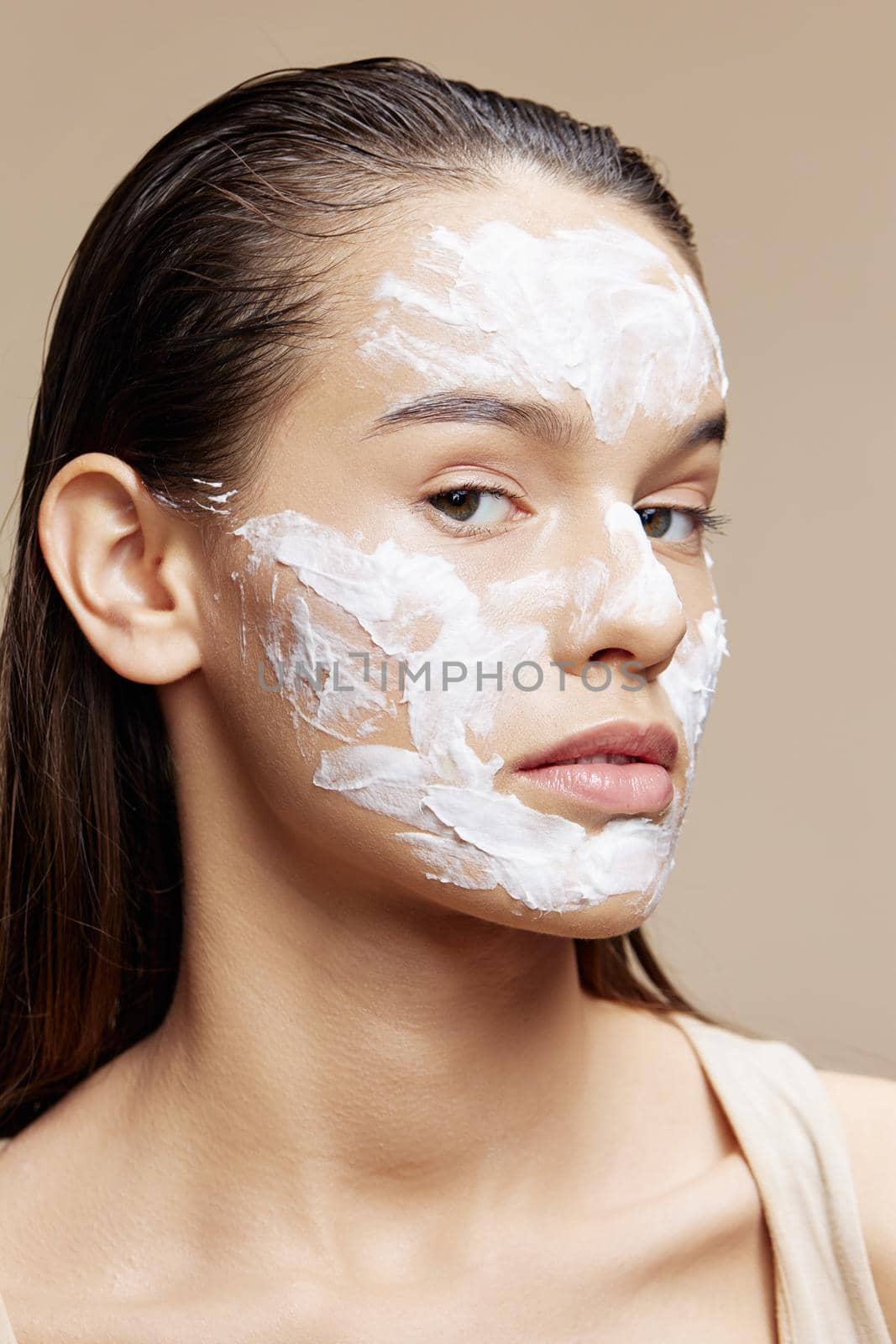 Beautiful Woman applying a soothing face mask skin care beige background. High quality photo