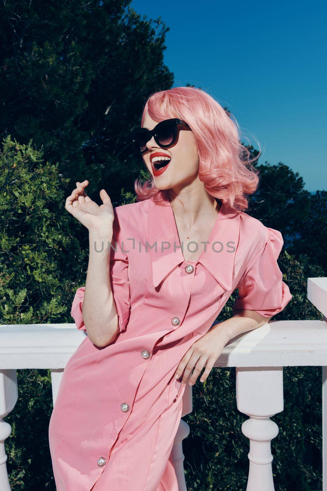 portrait of a young beautiful woman pink dress modern style stands near the railing sunny day. High quality photo