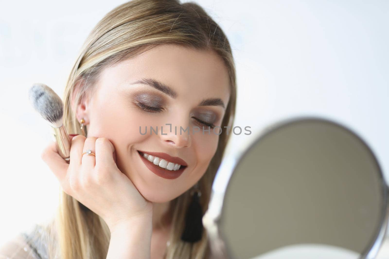 Portrait of elegant beautiful female with charming smile wearing makeup, glamour blonde lady visagist holding eye shadows brush. Mua, beauty, art concept