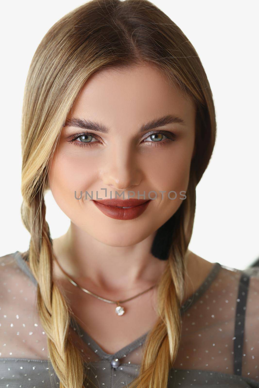Portrait of pretty blonde woman model with braids and luxury makeup posing in studio. Young female with tricky facial expression. Emotion, modeling concept