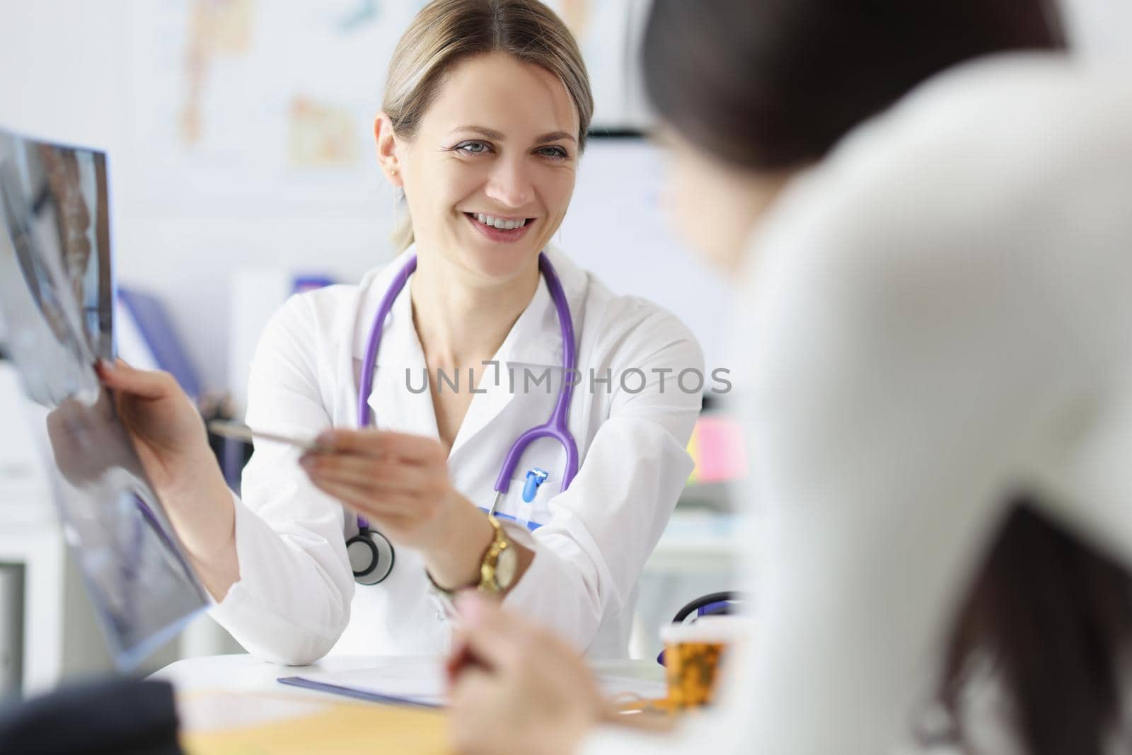 Portrait of female doctor show x ray result to patient and explain, professional specialist joking about disease. Medicine, healthcare, appointment concept