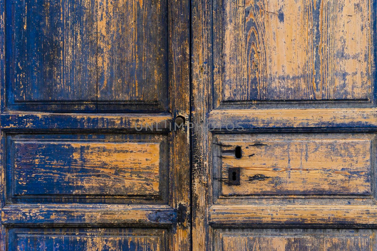 Detailed view of a wooden door with a lot of texture and the rest of blue paint on the wood background.