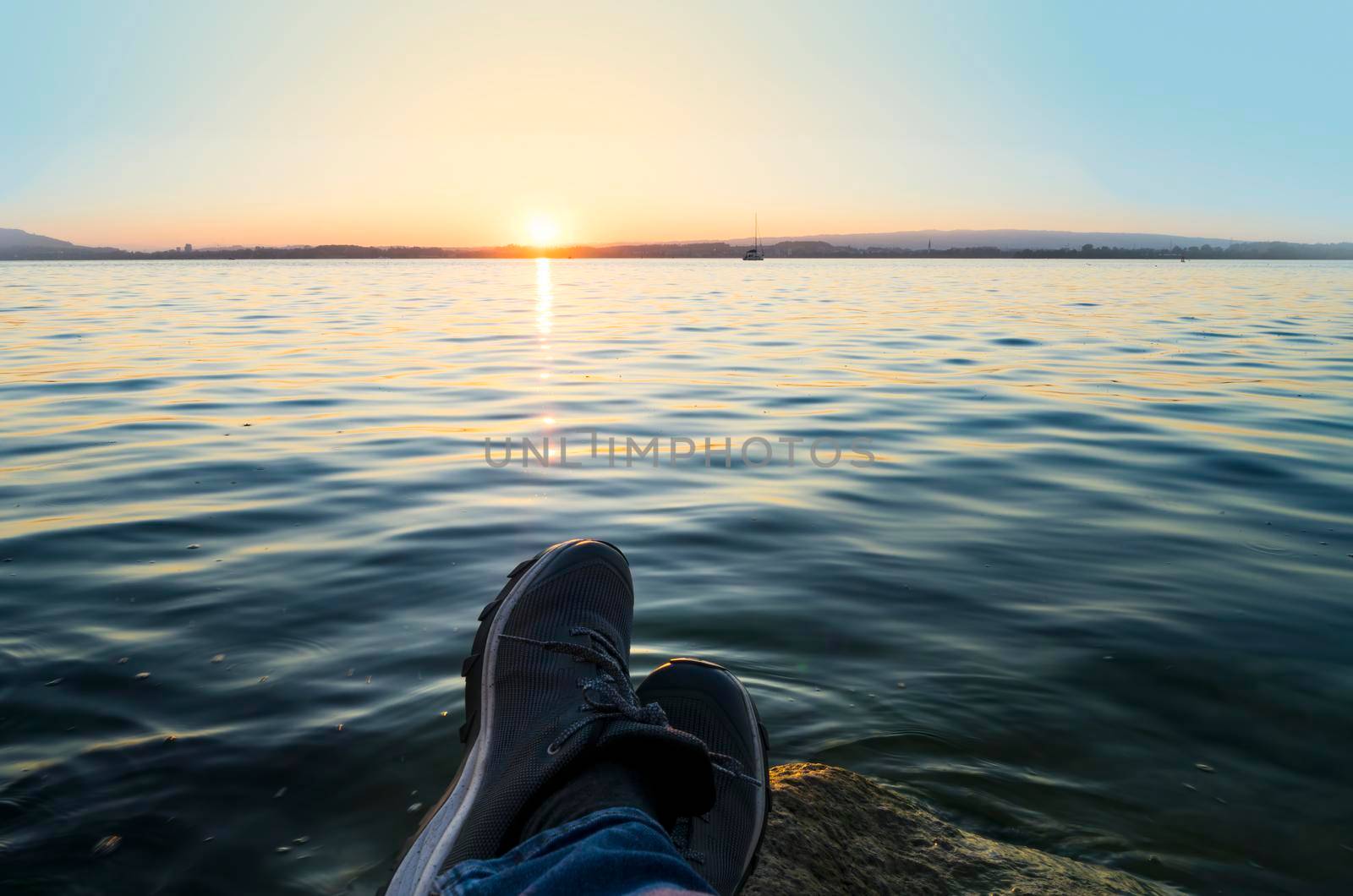 Sunset view of Lake Zugersee in the Swiss city of Zug with some slippers in the foreground of someone who is enjoying the sunset.