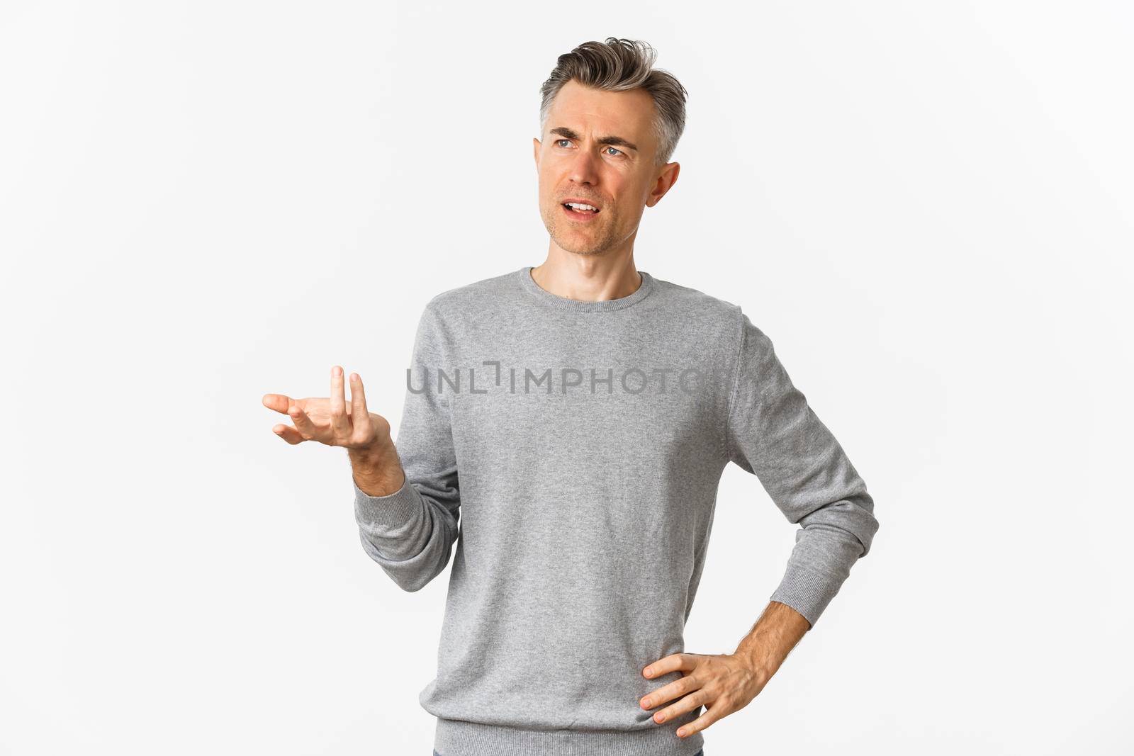 Image of confused middle-aged man cant understand something, raising hand and looking puzzled left, standing clueless over white background.