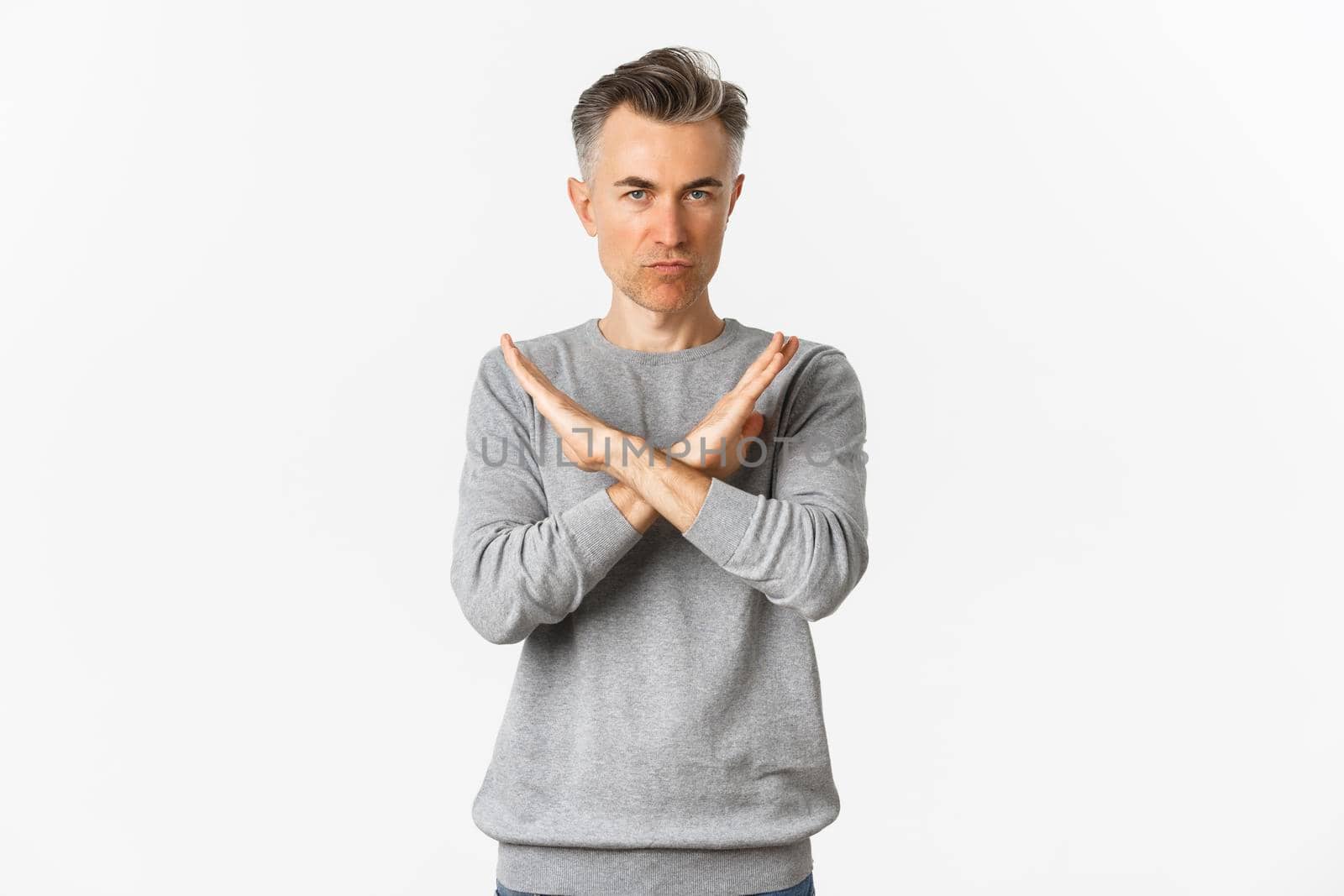Image of angry middle-aged man looking serious, making cross gesture to stop something bad, telling no, prohibit action, standing over white background.