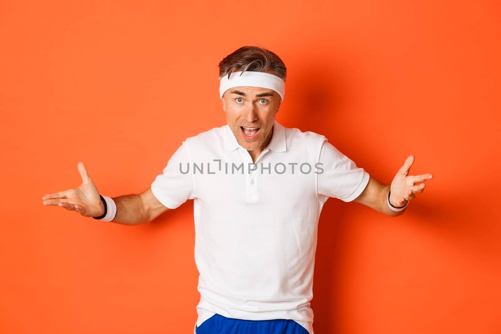 Concept of workout, sports and lifestyle. Portrait of confused middle-aged sportsman complaining, spread hands sideways and looking puzzled, cant understand something, orange background.