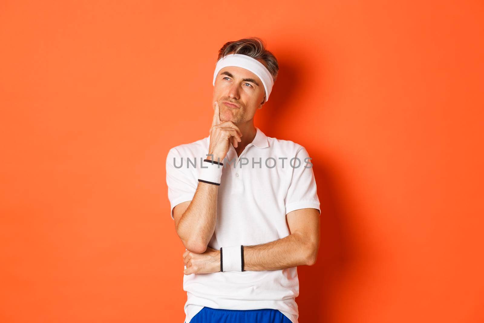 Concept of workout, sports and lifestyle. Portrait of thoughtful middle-aged man in fitness clothes, thinking about something, making decision over orange background.