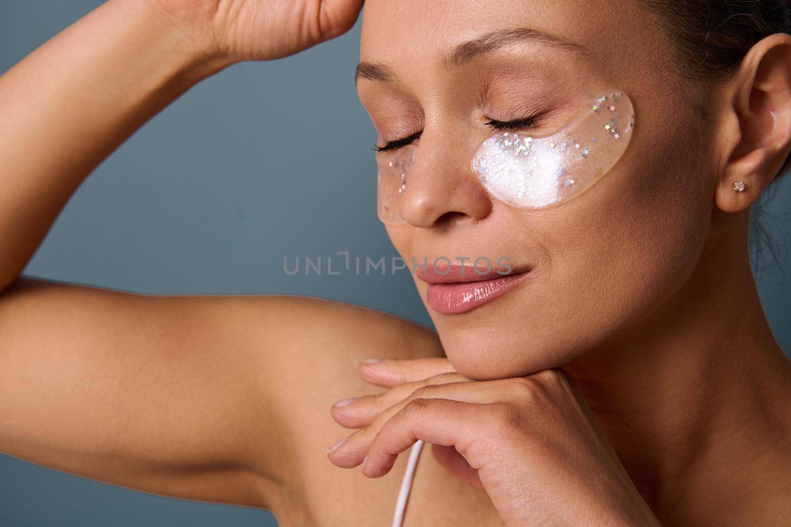 Head shot of a young beautiful woman with perfect glowing skin and natural makeup posing for the camera with medical collagen patches under her eyes to reduce fatigue and puffiness. Skin care concept by artgf