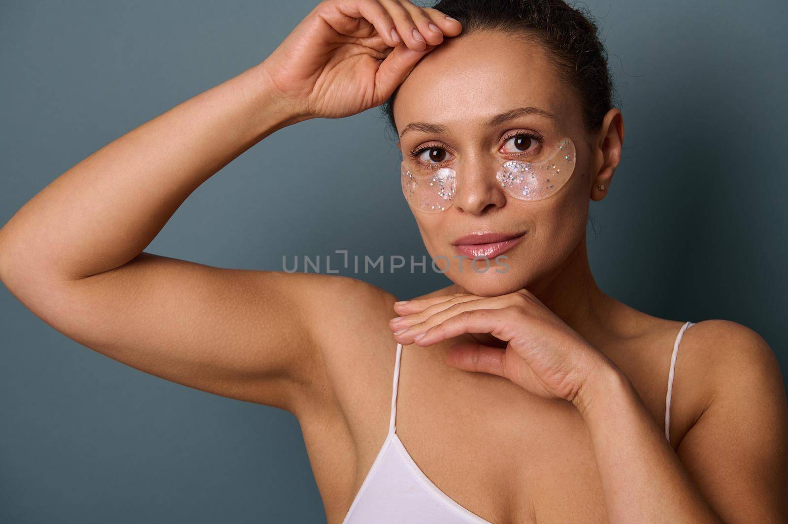 Attractive woman with anti-fatigue under-eye mask looking at camera posing against gray background. Skin care, hydrogel collagen patches, fabric mask under eyes to reduce eye bags and puffiness by artgf