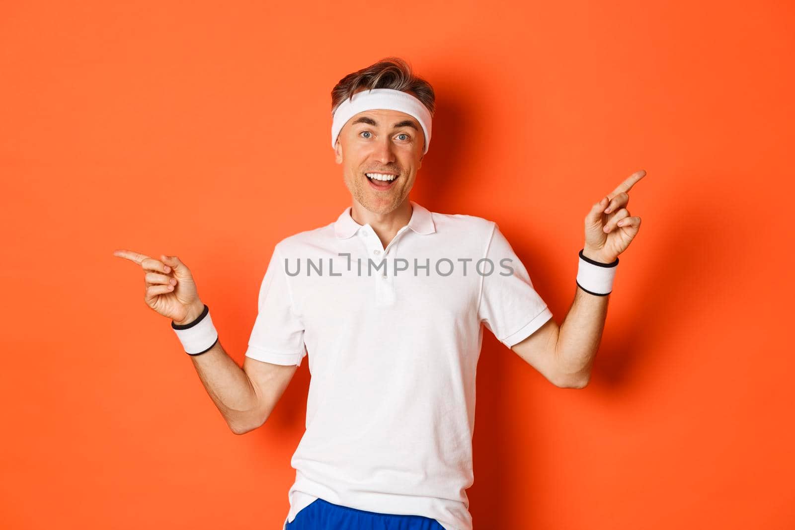 Concept of sport, fitness and lifestyle. Cheerful middle-aged sportsman with headband, smiling happy and pointing fingers sideways, showing left and right copy space.