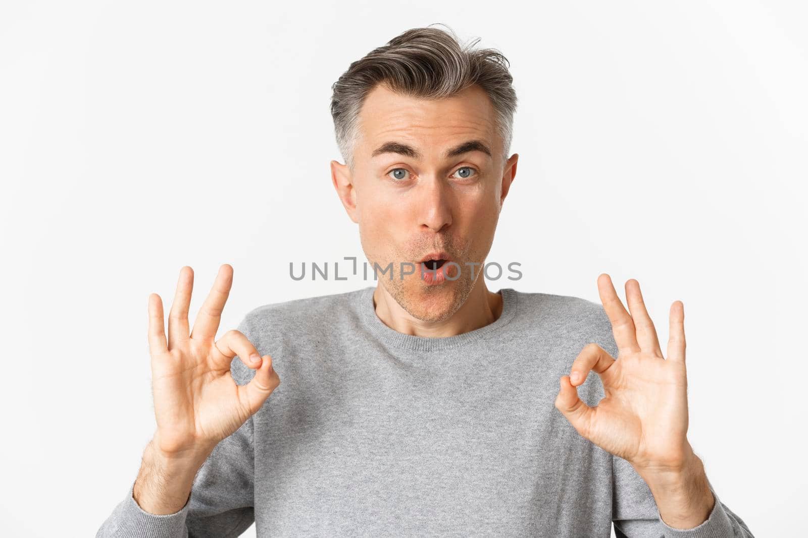 Close-up of impressed middle-aged guy, showing okay signs in approval, like something good, recommending product, standing over white background.