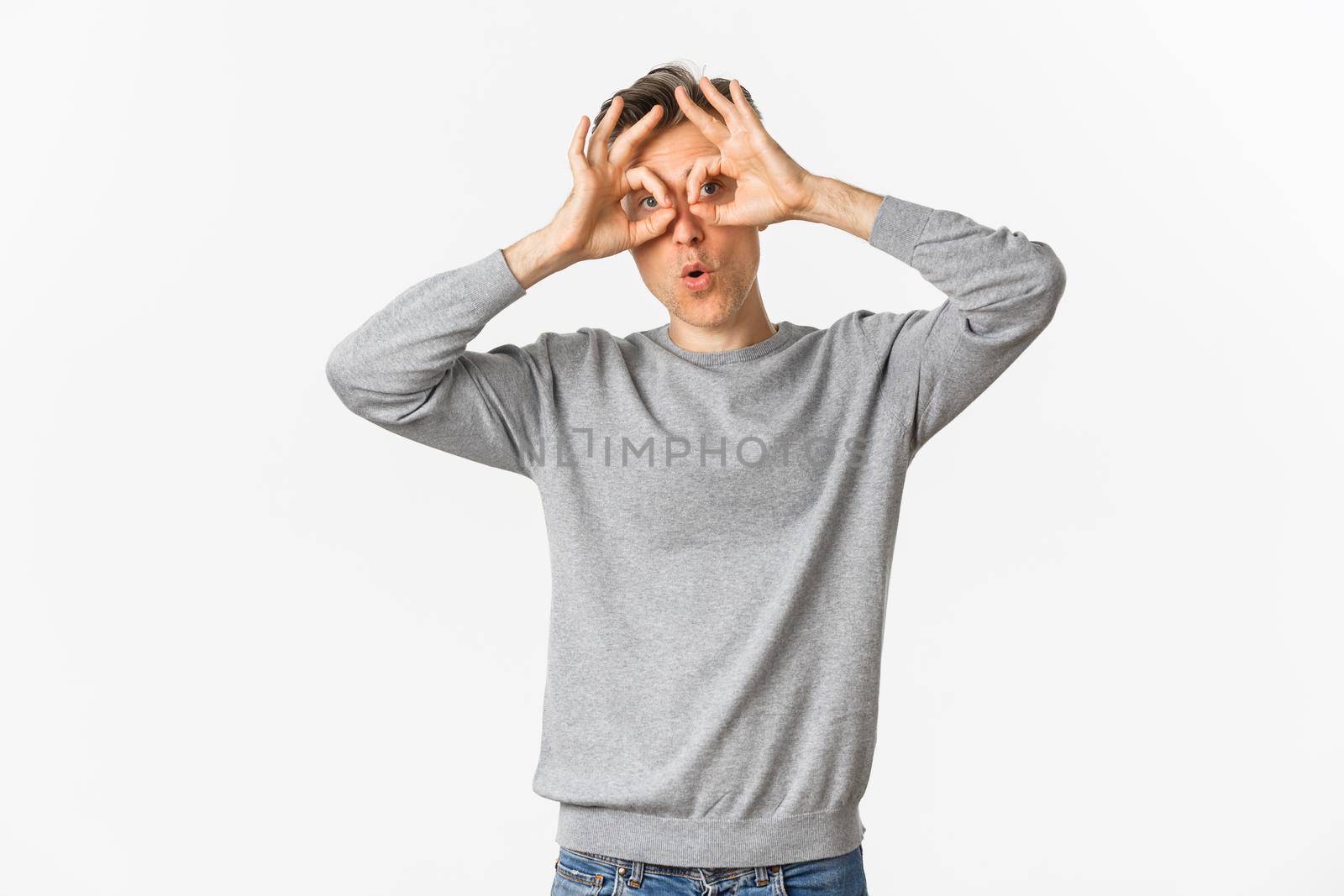 Portrait of funny middle-aged guy making faces, showing hand glasses around eyes and fooling around, standing over white background.