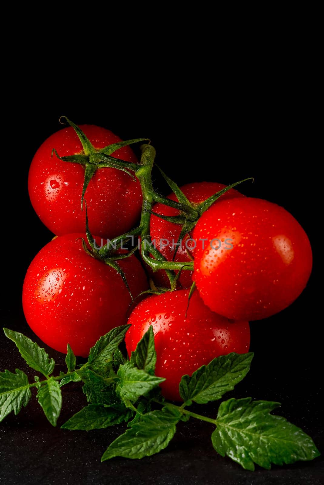 Organic tomatoes on the black table in low key, with water drops