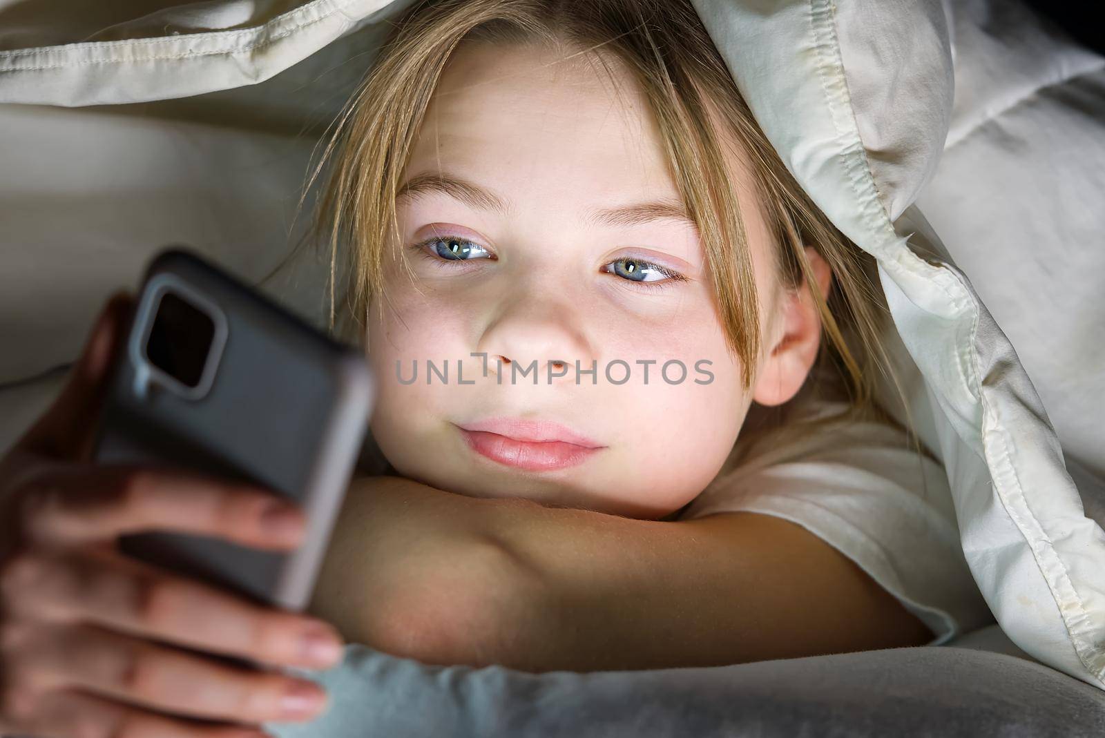 Portrait of girl with mobile phone under blanket at night. Gadget night. Social media addiction. Online communication. by PhotoTime