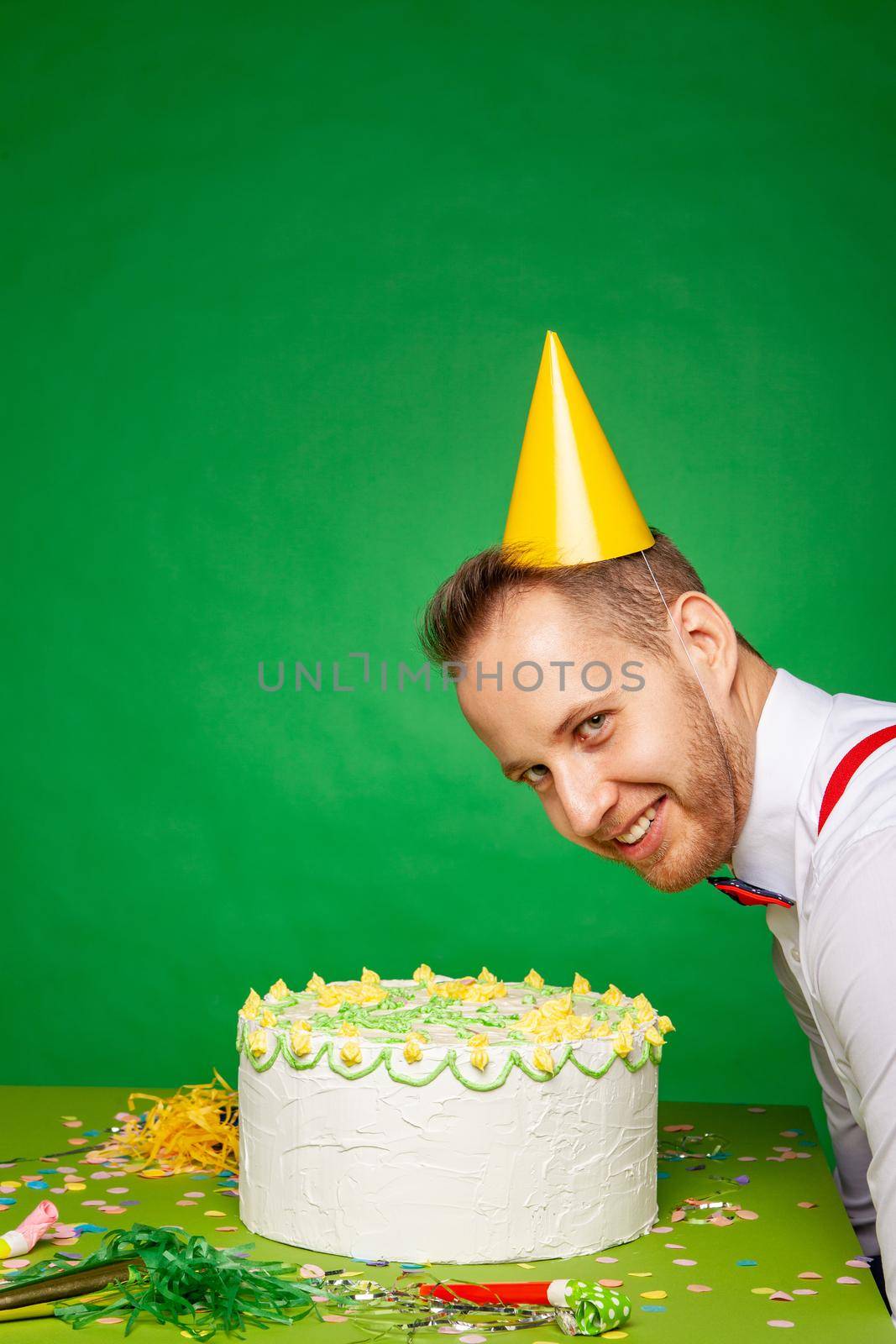Smiling man in party hat with birthday cake in studio by Julenochek