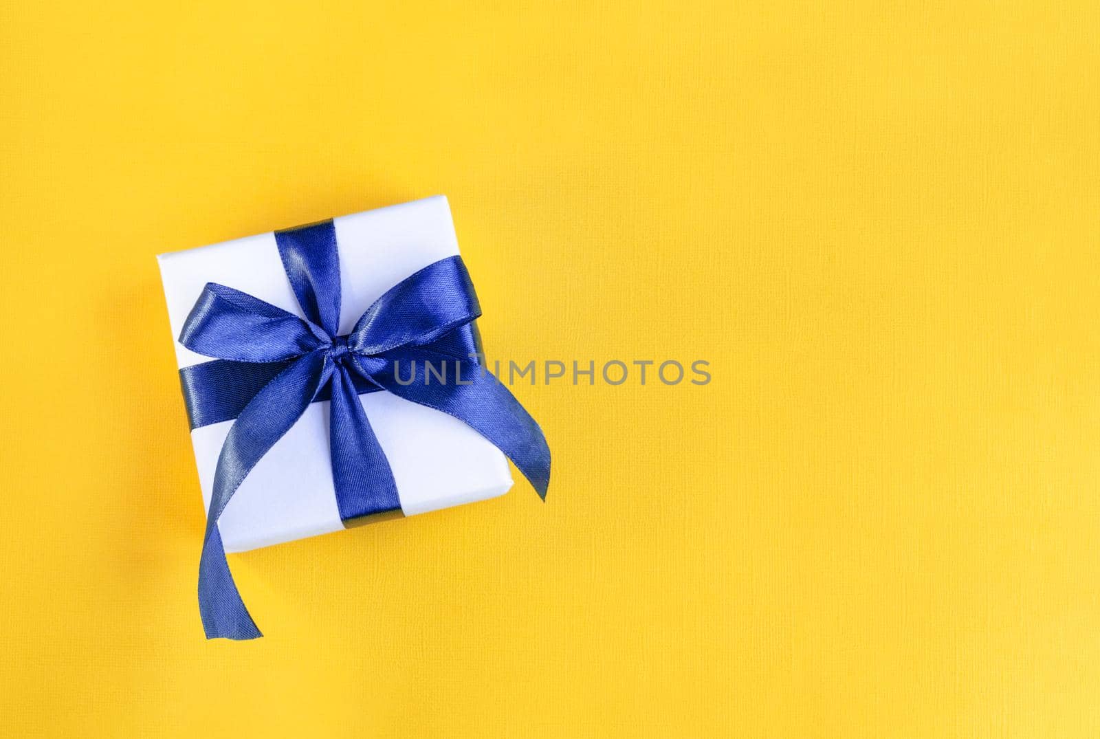 Banner of Gift wrapped in white paper with a blue bow made of satin on festive yellow orange background. St Valentines day, Birthday, New Year, Christmas, Mothers or Fathers day concept