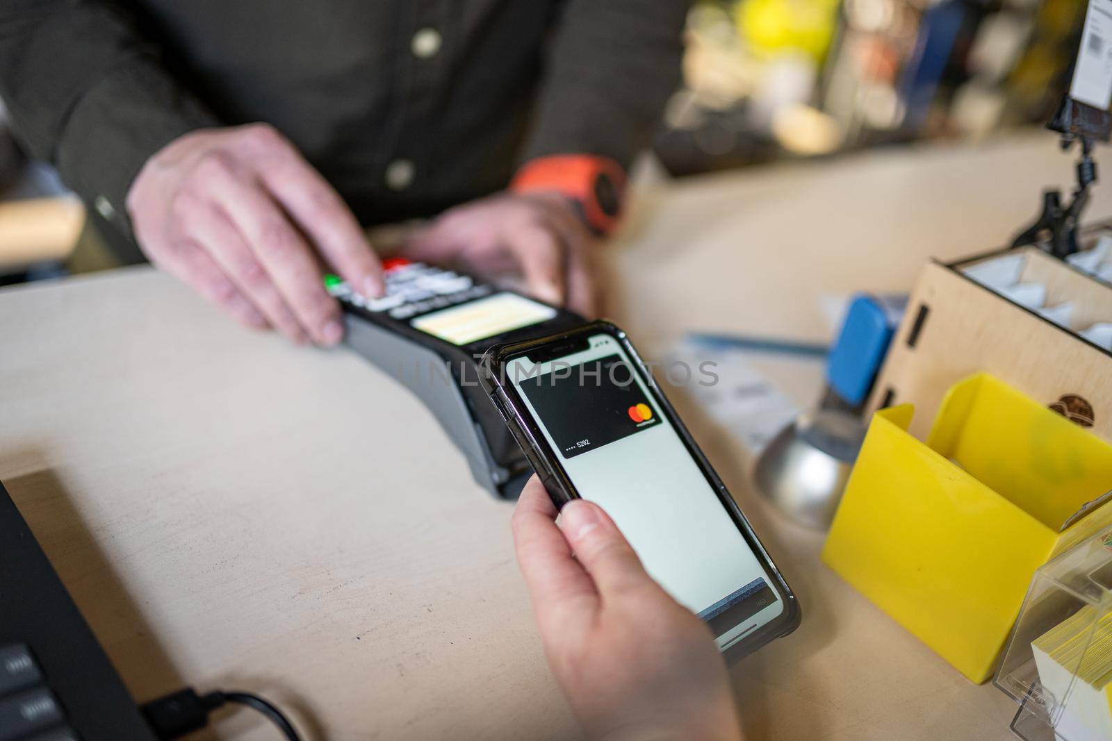 Close-up of woman making payment through NFC. Woman pays via payment terminal and mobile phone. Cashier hand holding credit card reader machine while client holding phone for NFC payment.