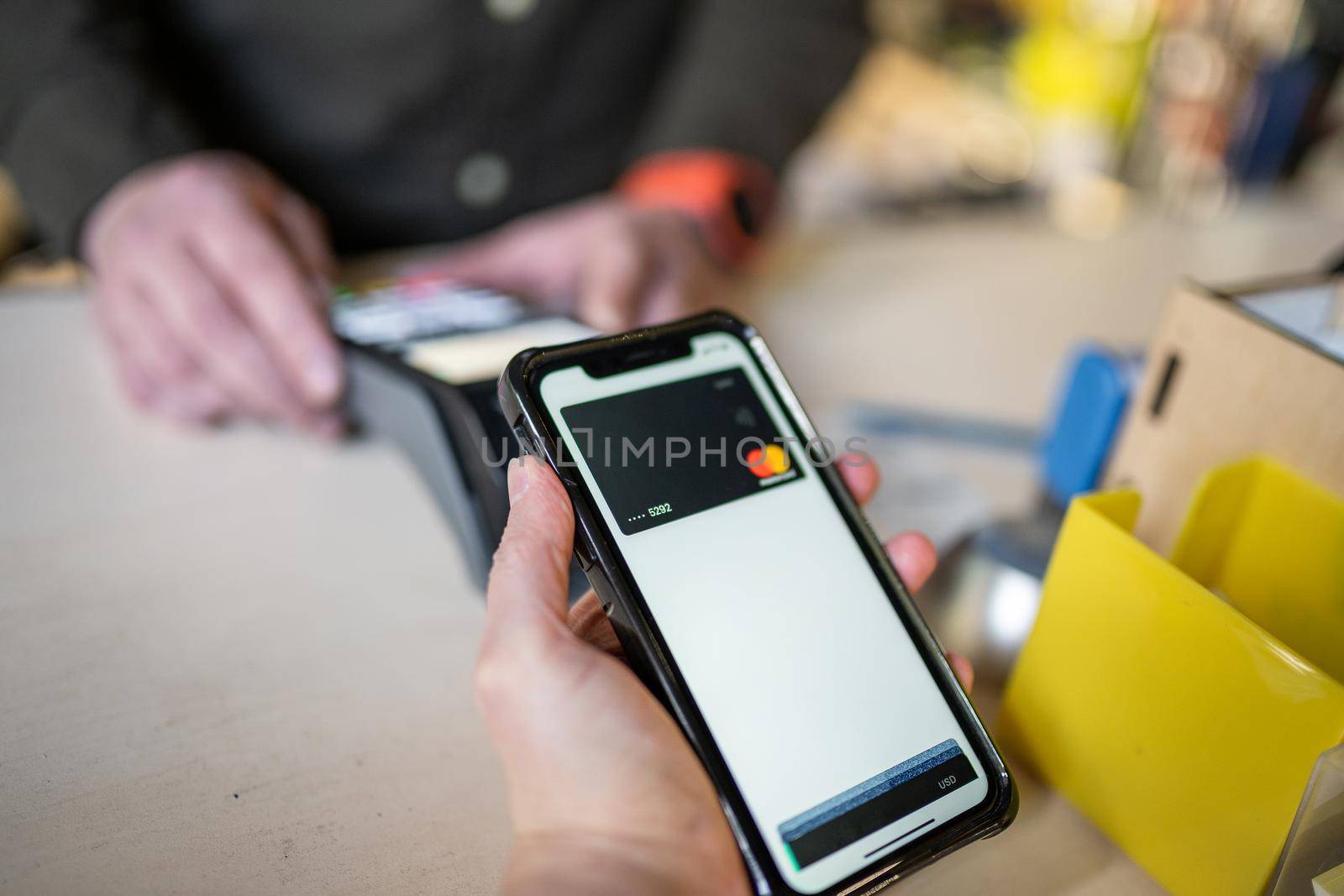 Cropped view of woman standing on checkout, paying for shopping in store, using modern smartphone while cashier holding NFC terminal in hand. Wireless payment using smartphone and NFC technology.