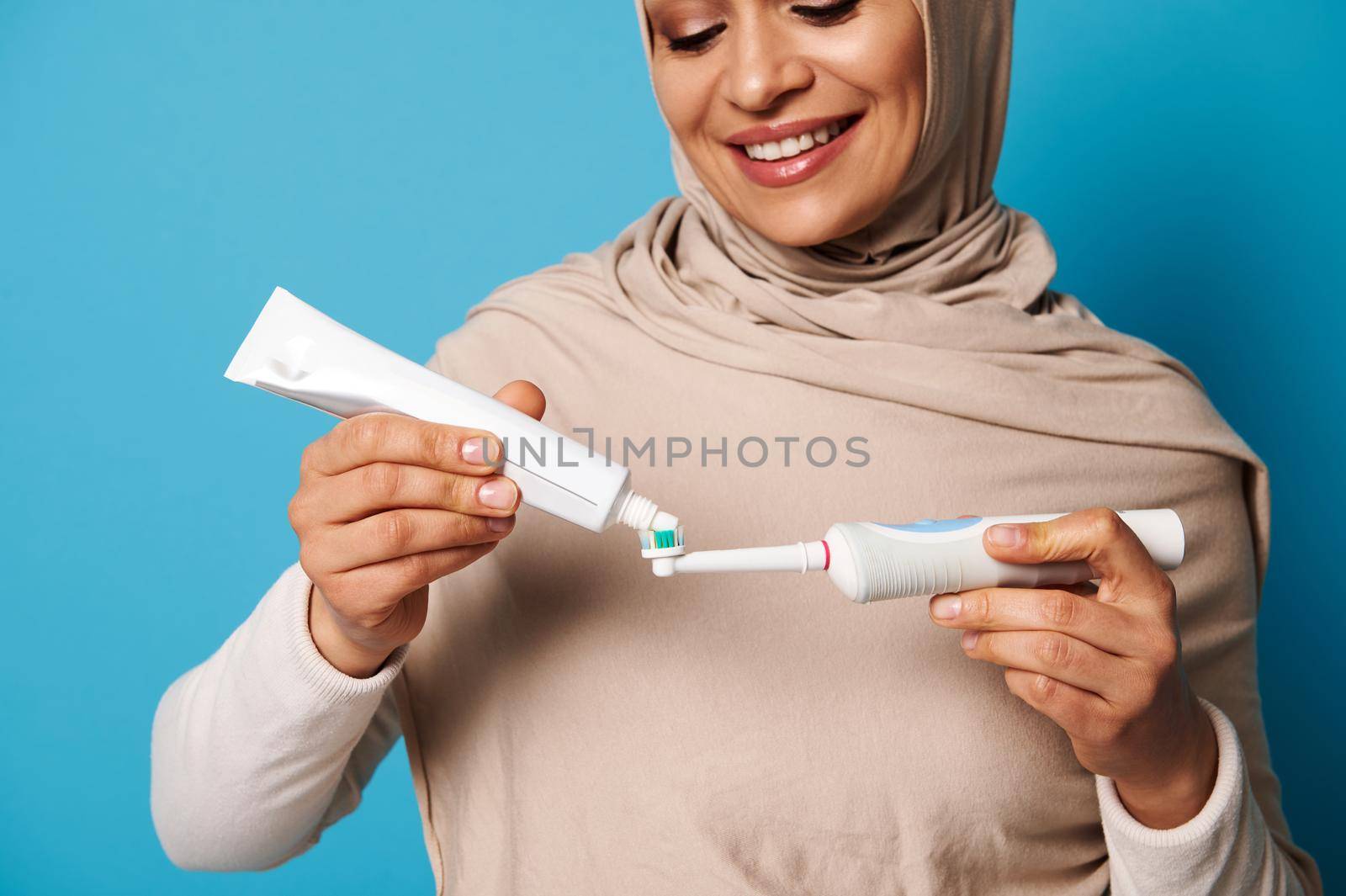Close-up woman with a beautiful smile squeezes toothpaste from a tube into a toothbrush. Concept of healthy habits and oral care. Blue background, copy space