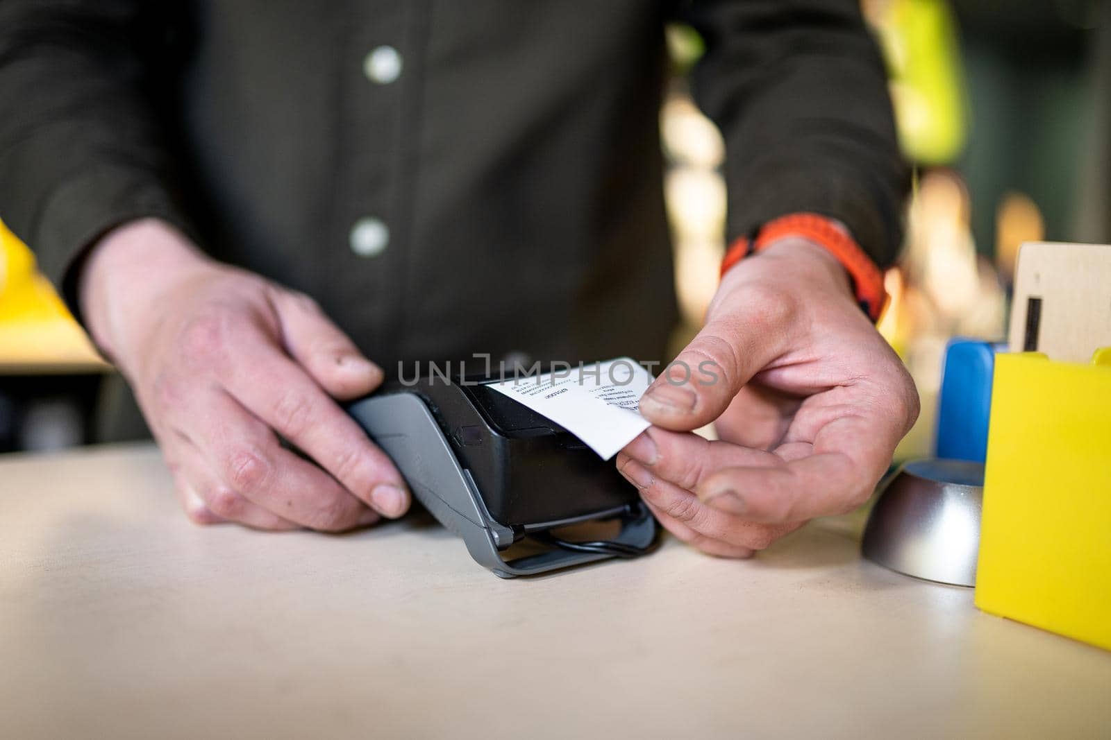 Man holds payment terminal while holding receipt for completing a purchase. Hands close up and side view. Concept of NFC, business and banking transaction. Close up of payment device, card machine by Tomashevska