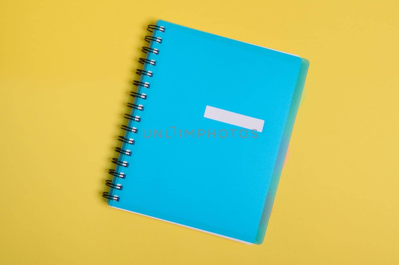 Close-up of a blue colorful organizer, notepad with empty blank sheet for text, isolated on yellow background with copy space. Flat lay by artgf