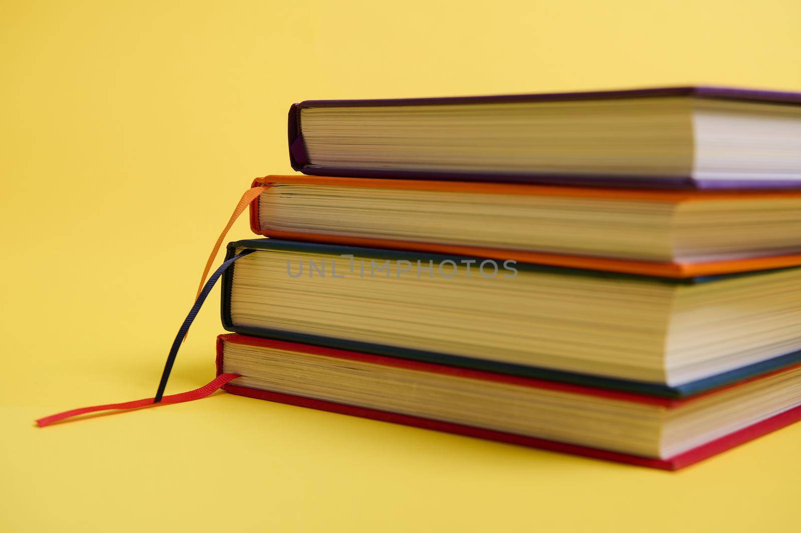 Close-up studio shot of a stack of multicolored books on yellow surface background with copy space for text. Teacher's Day concept, Knowledge, literature ,reading, erudition by artgf